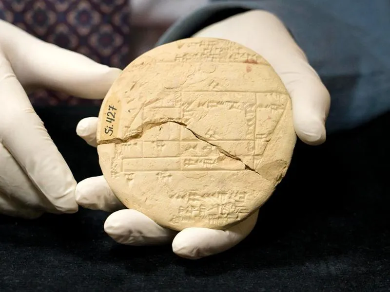 Gloved hands holding cuneiform clay tablet
