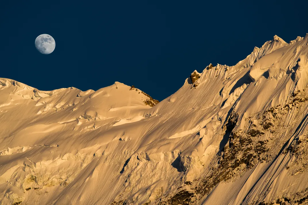 sun set on a snow-covered mountain with the moon in the sky