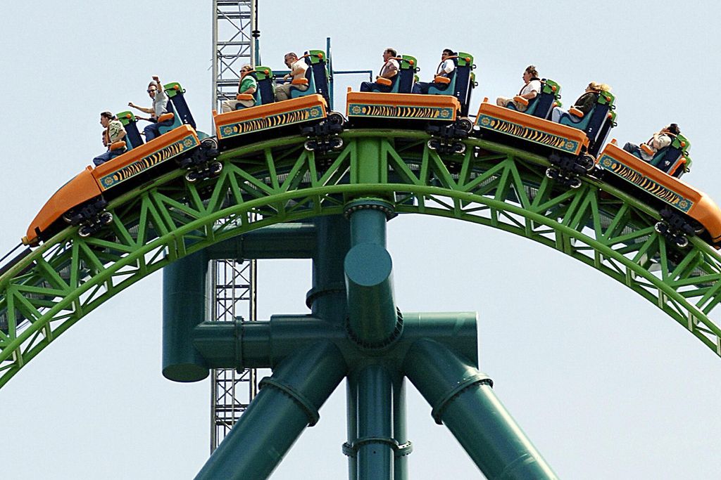People riding orange carts at the top of a green roller coaster