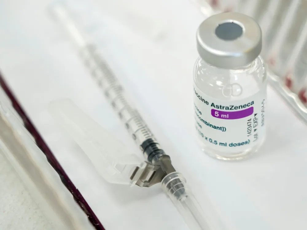 A vial of AstraZeneca vaccine sits on a white surface next to a capped syringe 