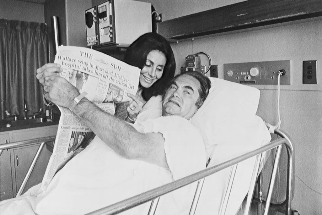 After his shooting, a hospitalized Wallace holds up a newspaper touting his victories in the Maryland and Michigan Democratic presidential primaries.