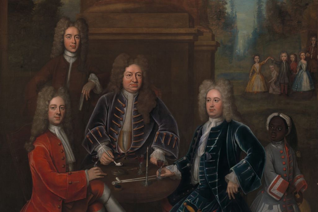 A group portrait of four white men sitting and standing around a table, smoking and drinking wine, while a small group of white children play in the distance and a Black child wearing a padlocked collar serves them wine