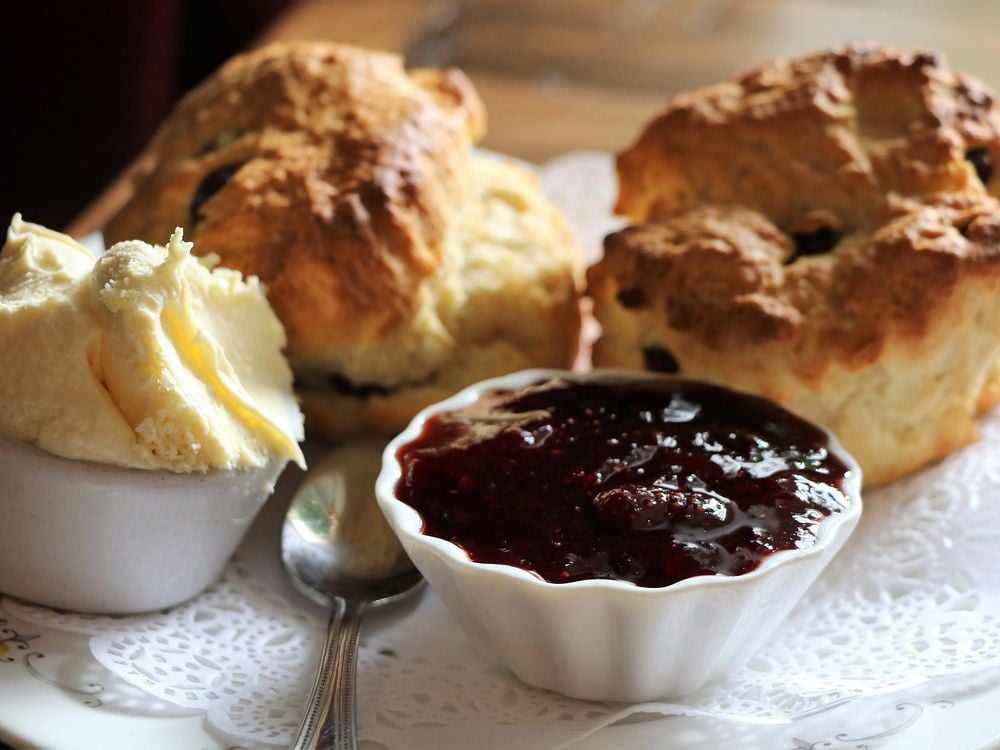 Two golden scones on a plate with clotted cream and strawberry jam