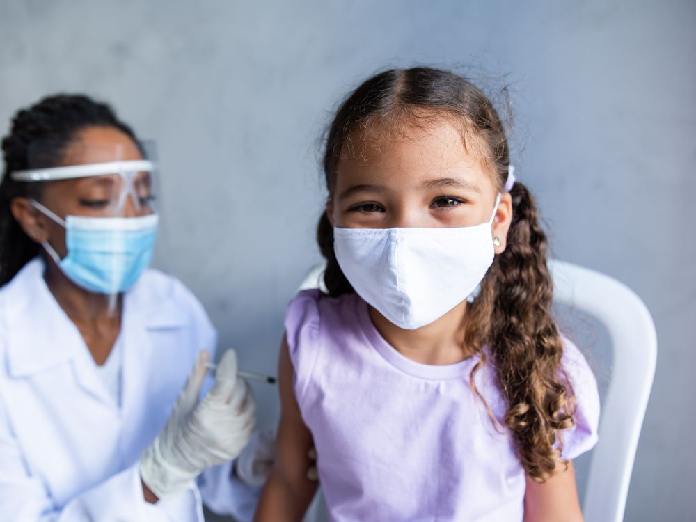 An elementary school aged girl wearing a face mask gets a vaccine