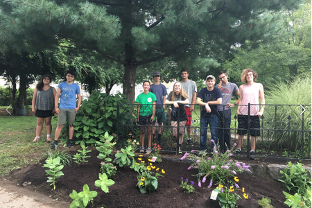 A group of young people stand in front of a pollinator garden in Lowell, MA