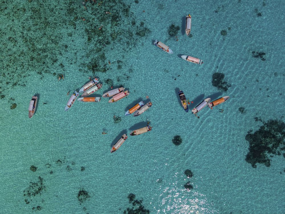 Tourist boats float above the turquoise shallows near Zanzibar, their bright colors standing out against the clear water. Photographed from above, the scene captures the island’s growing tourism and the traditional vessels that now carry visitors along the coast.