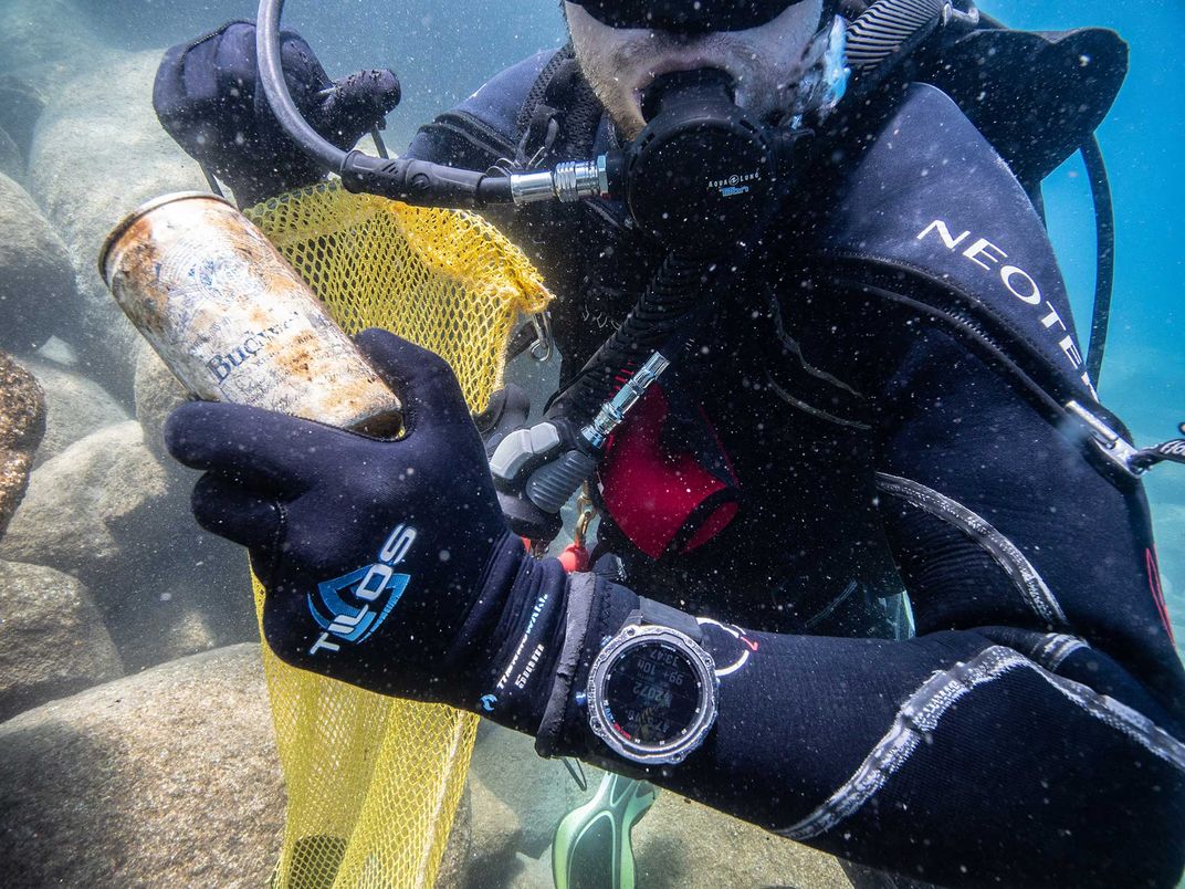 Scuba diver holding rusty beer can underwater