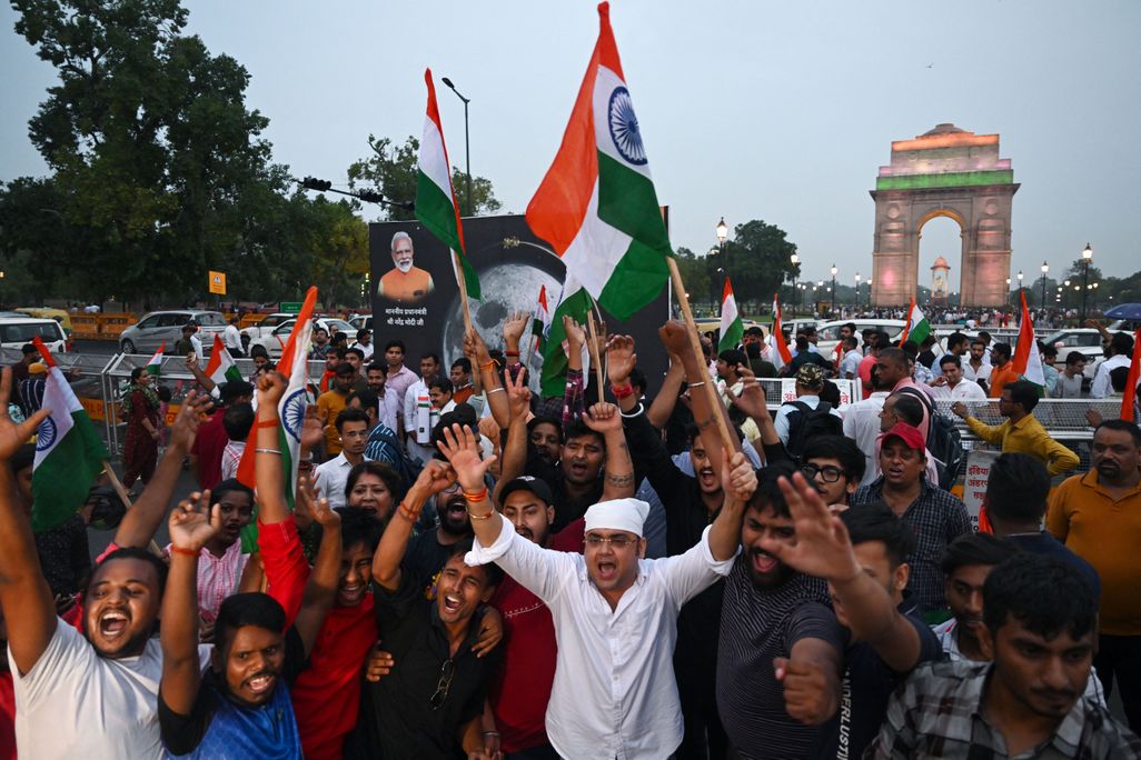 People hold their arms in the air and wave Indian flags as they celebrate the moon landing