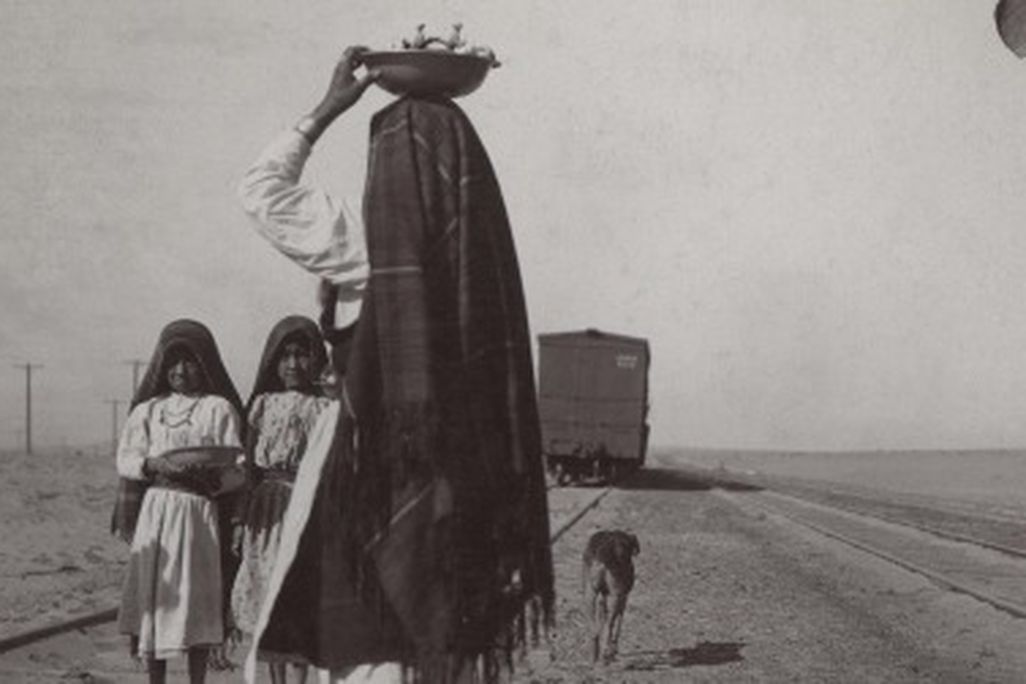 An Isleta woman and her children sell goods alongside a train track, circa late 1880s to early 1900s