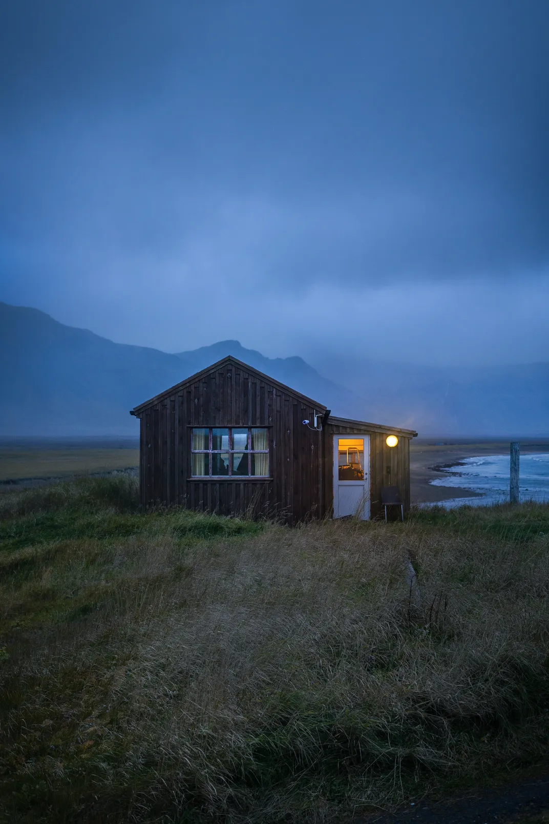 6 – Eine schwach beleuchtete Hütte steht am Ufer der Westküste Islands.
