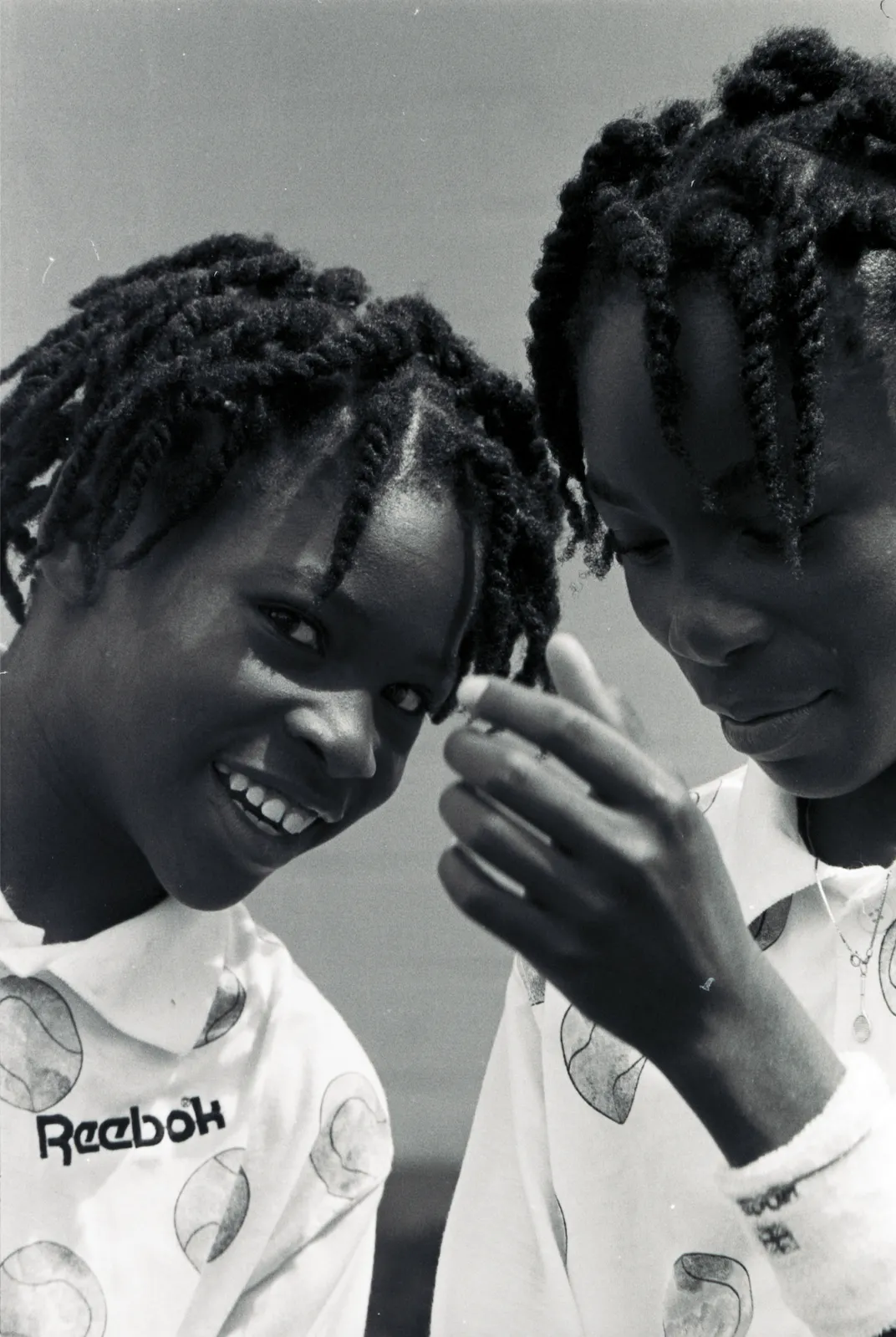 Serena (left) leans in toward her sister Venus (right) and looks at the camera with a smile on her face.