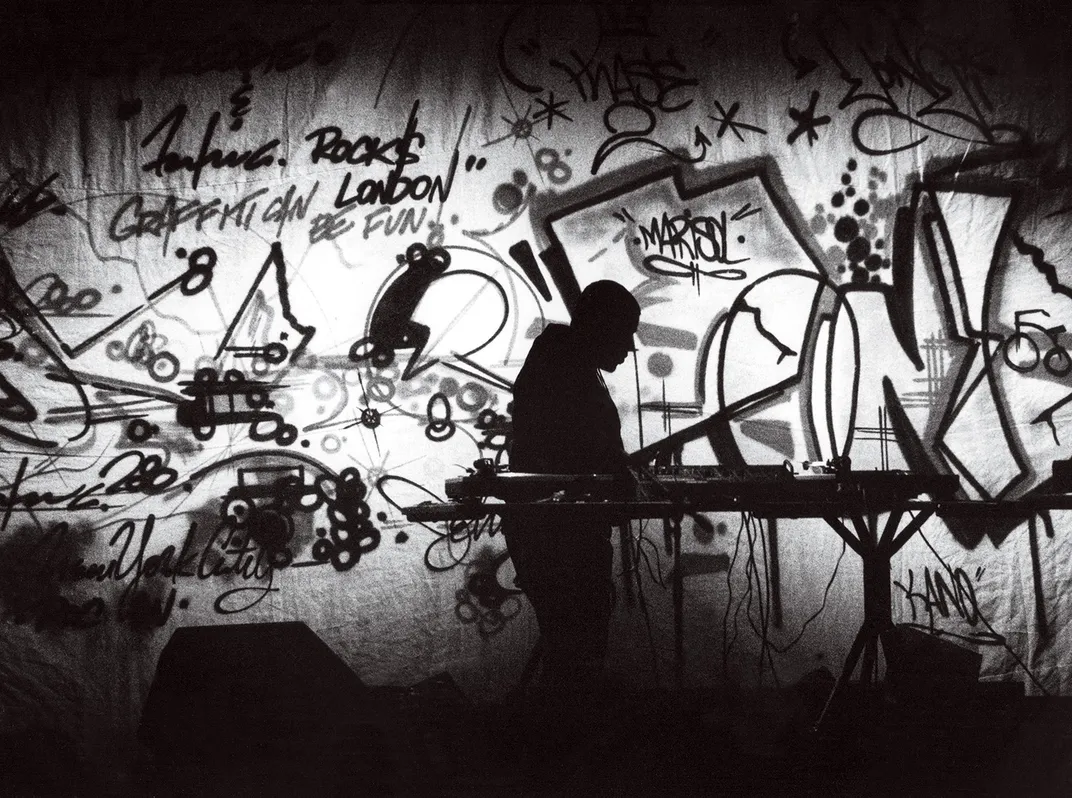 a black and white photograph of a DJ on stage surrounded by graffiti art
