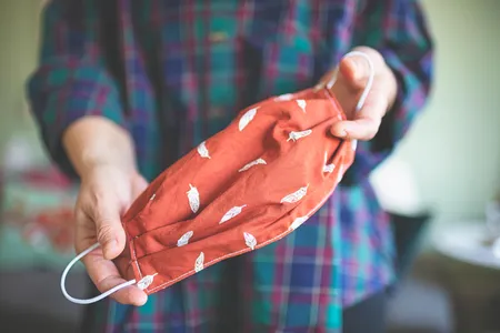 A person holds a sewn handmade fabric mask. 