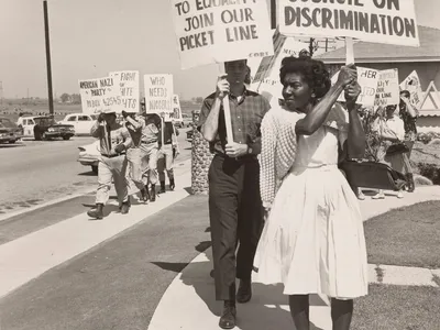 Activists picketing at a demonstration for housing equality while uniformed American Nazi Party members counterprotest in the background with signs displaying anti-integration slogans and racist epithets.
