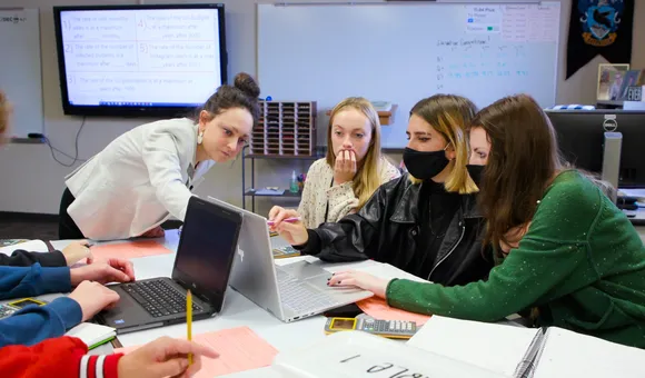 Peterson wears a bun and blazer pointing towards a computer screen with her students