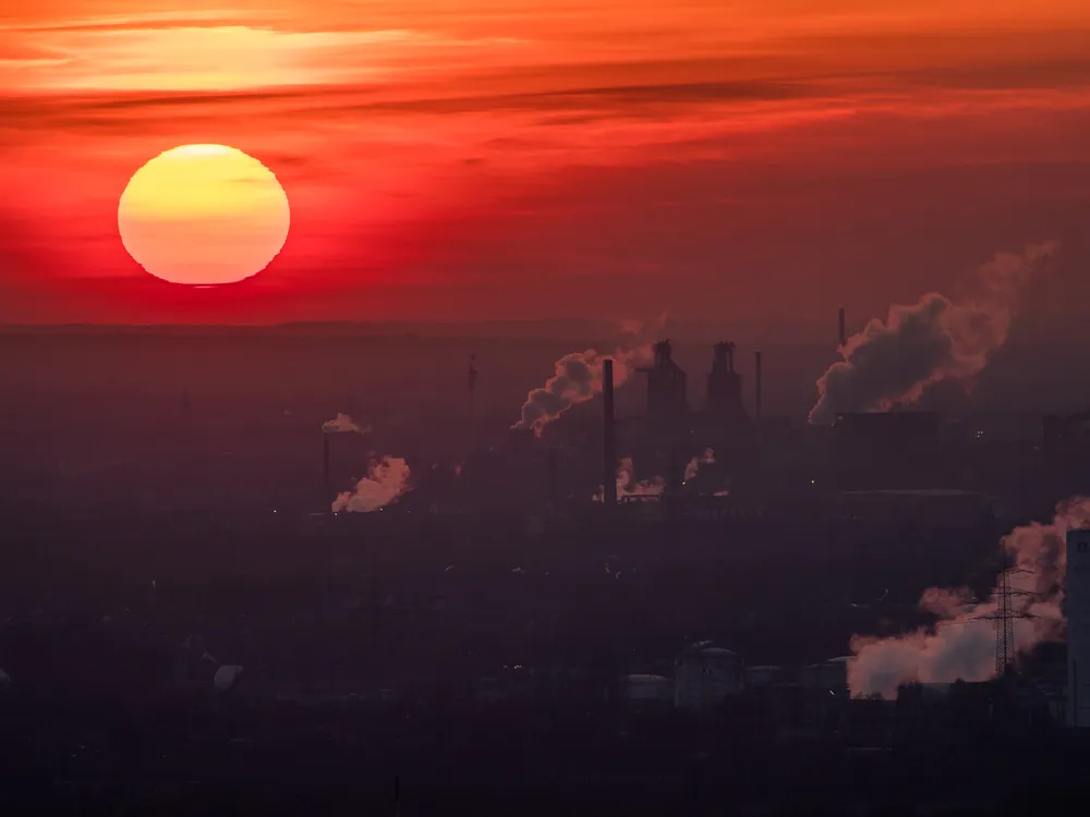 A setting sun over emissions billowing from buildings on the ground.