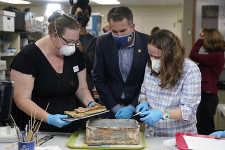 Virignia Governor Ralph Northam (center) looks on as conservators Kate Ridgway (left) and Sue Donovon (right) remove the time capsule's contents.