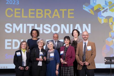 Group of Smithsonian Education awardees with leadership standing in front of a large screen that says "Celebrate Smithsonian Education"
