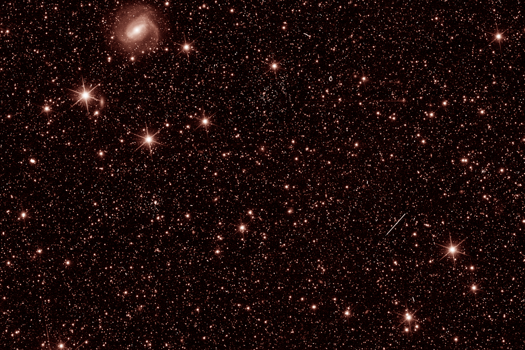 An image of outer space showing distant stars and galaxies in a light red color