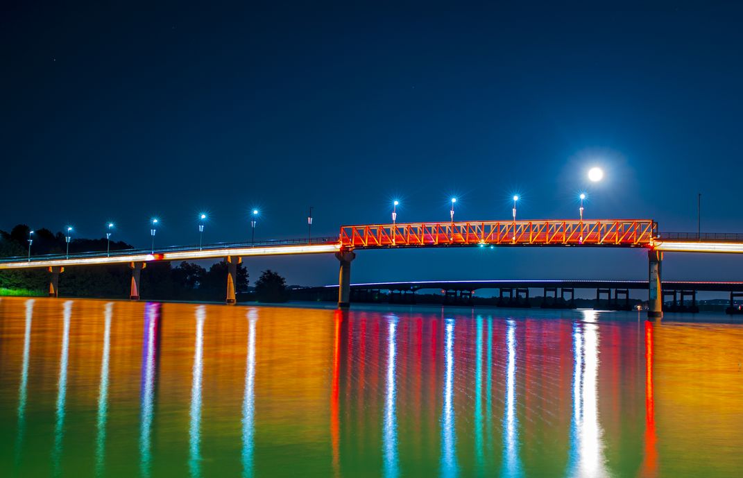 The colors from the bridge and the glow of the moon entertain the night