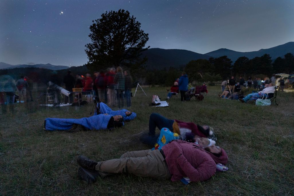 A crowd of people are laying on the ground in a grassy field at night with mountains in the background