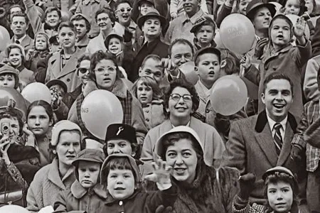 A crowd of people cheering and waving at a parade, circa 1955.