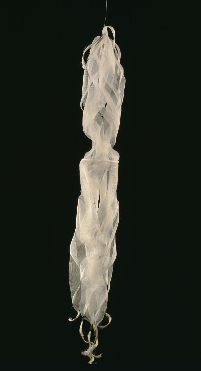 A white, hanging fiber sculpture against a black background