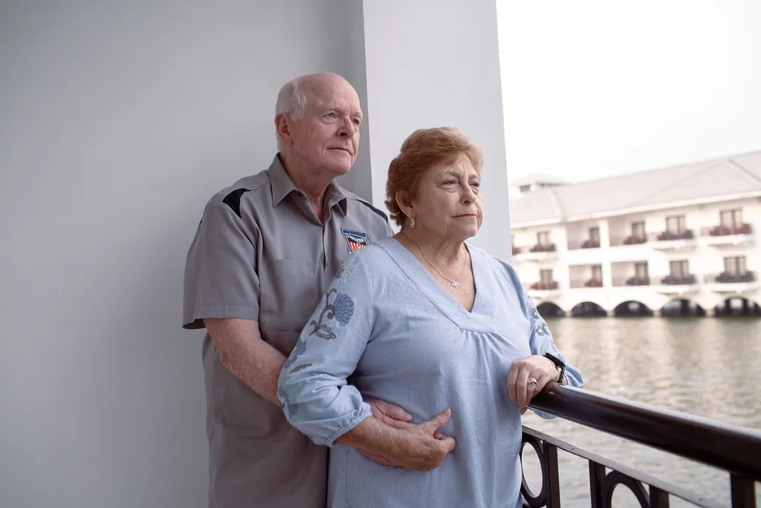 a couple stand for a portait on a hotel balcony next to water