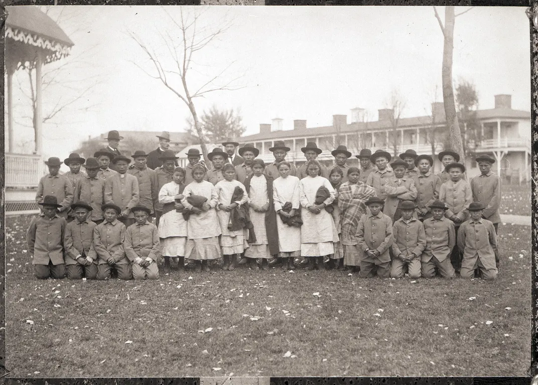 A group of Chiricahua Apache Indian youth, some dressed in white and some in military style uniforms on the grounds of the