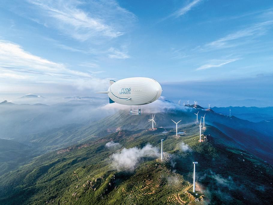 Concept art of the Flying Whales airship. A white airship with blue fins flies over green mountaintops covered with white windmills.