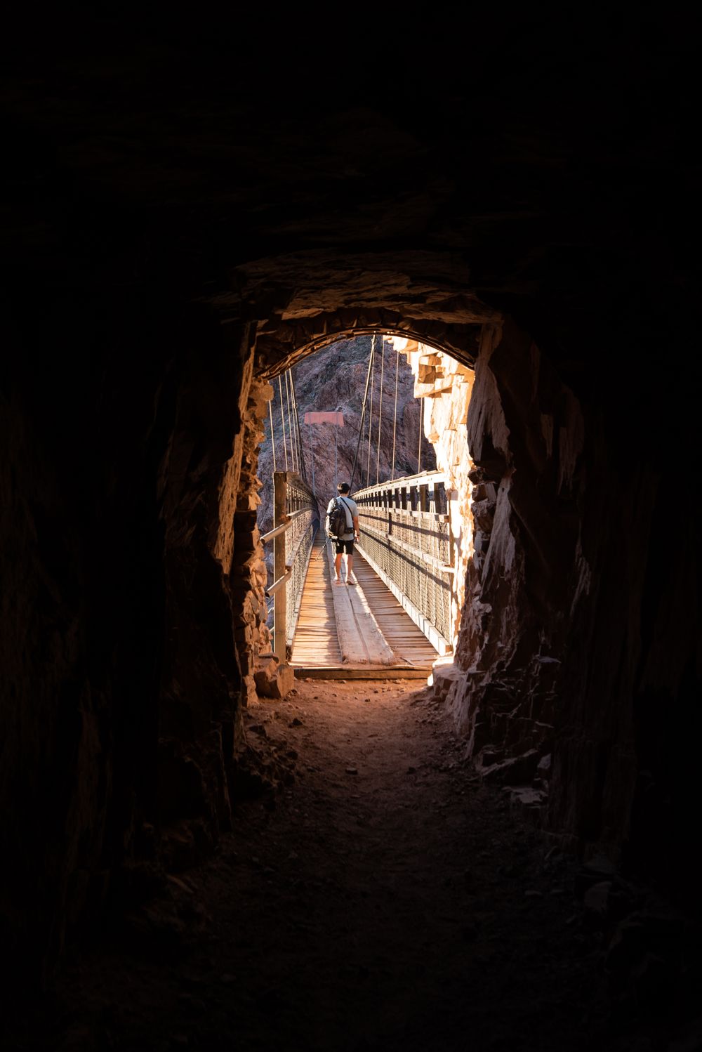 Finally nearing the end of our hike to the bottom of the Grand Canyon, my brother crossed the bridge in the light of the setting sun. I was a few steps behind in the darkness of the tunnel.