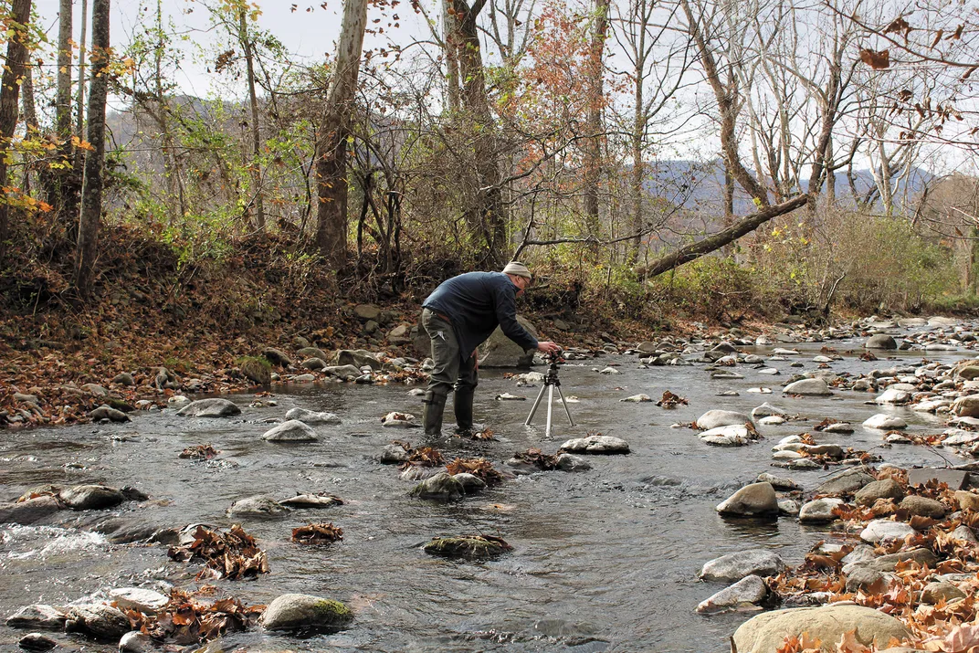 a man stands in a stream recording its sounds