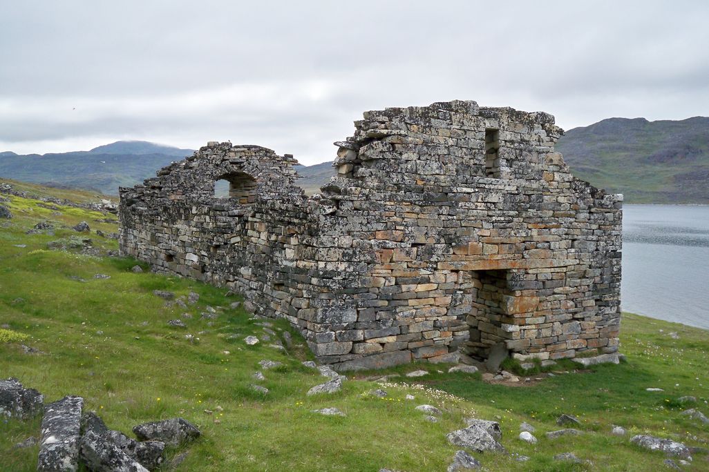 ruins of a gray and brown stone building on green landscape overlooking lake