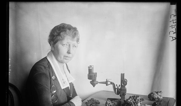 Black and white photo of Margaret W. Moodey sitting at a desk with a microscope and gemstones