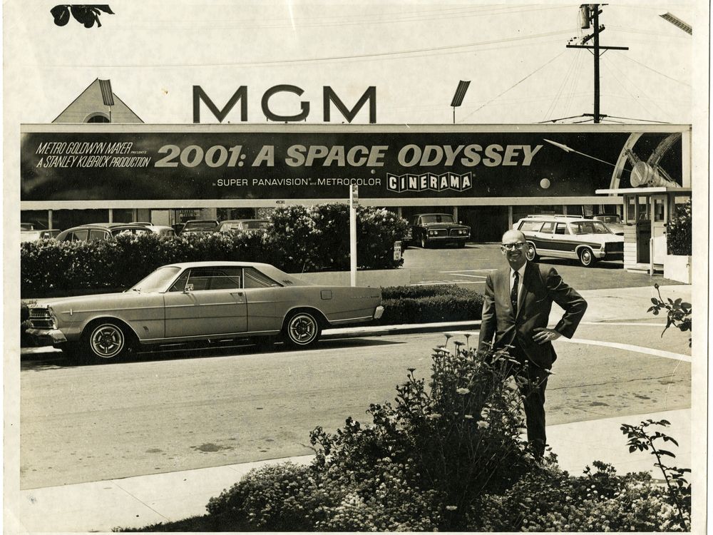 Arthur C. Clarke poses for a photo beneath a sign advertising the motion picture
