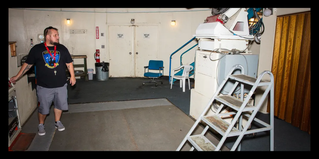 Rankin stands at the left, looking at white telescope equipment at the right, with a stepladder in front of it