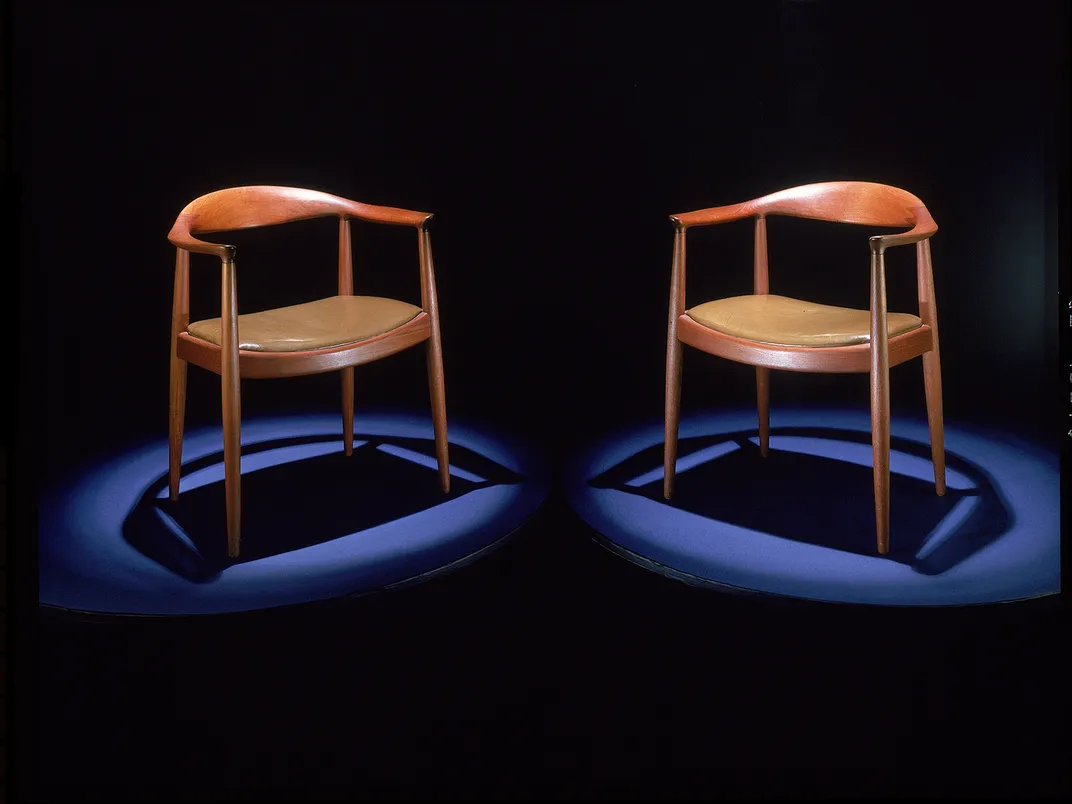 two wooden chairs angled towards each other are spotlit for the photograph