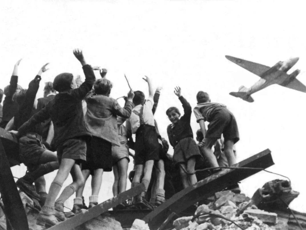 black and white image of a group of German children eagerly stretching their hands toward aircraft flying overhead.