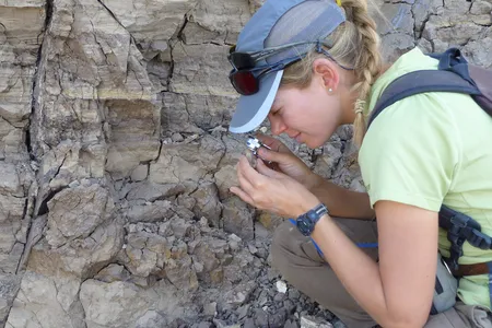 Using a geologist’s magnifying glass, Erin DiMaggio carefully scans a piece of volcanic ash in search of tiny minerals that hold the key to determining the age of nearby fossils.  