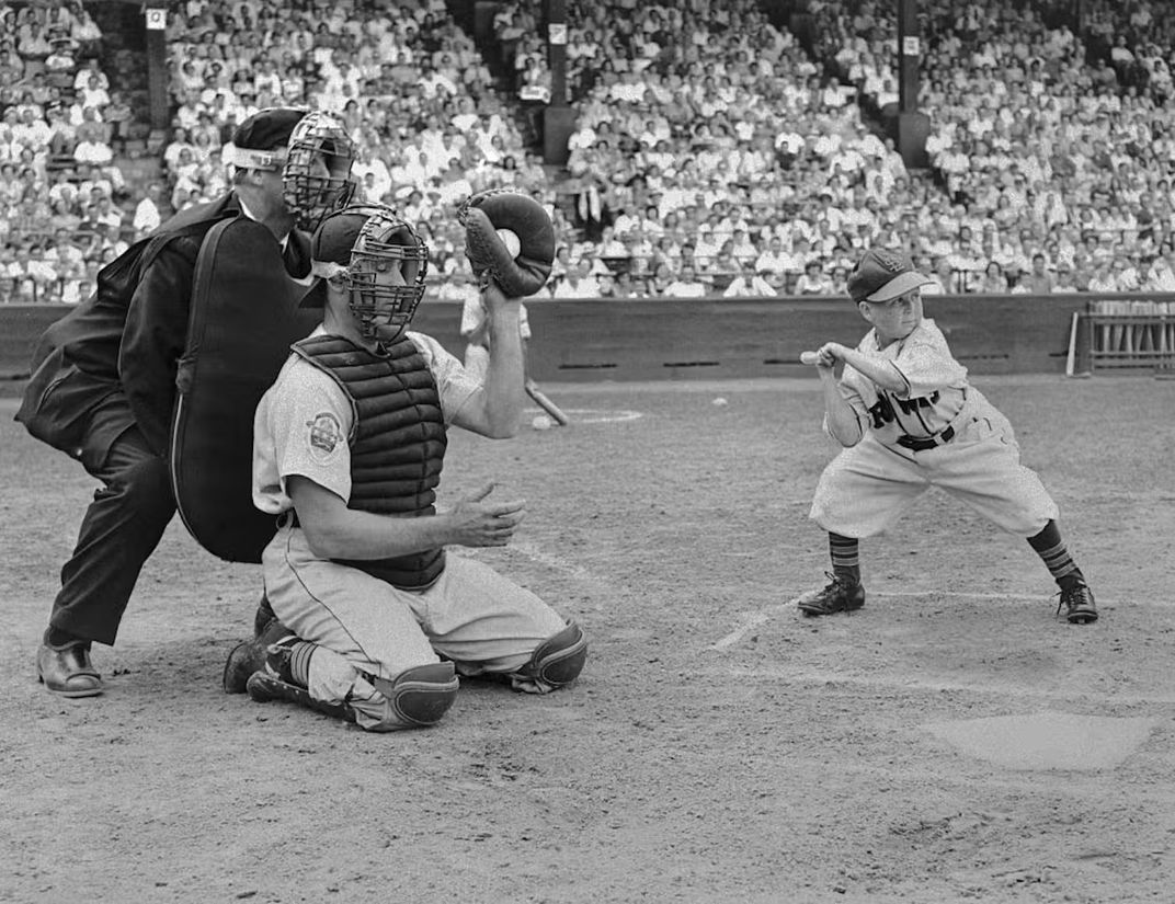 Eddie Gaedel up to bat. A catcher and umpire crouch behind home plate.