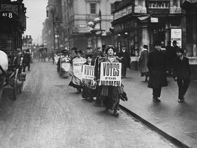Suffragettes protest along a London street wearing sandwich boards in 1912.