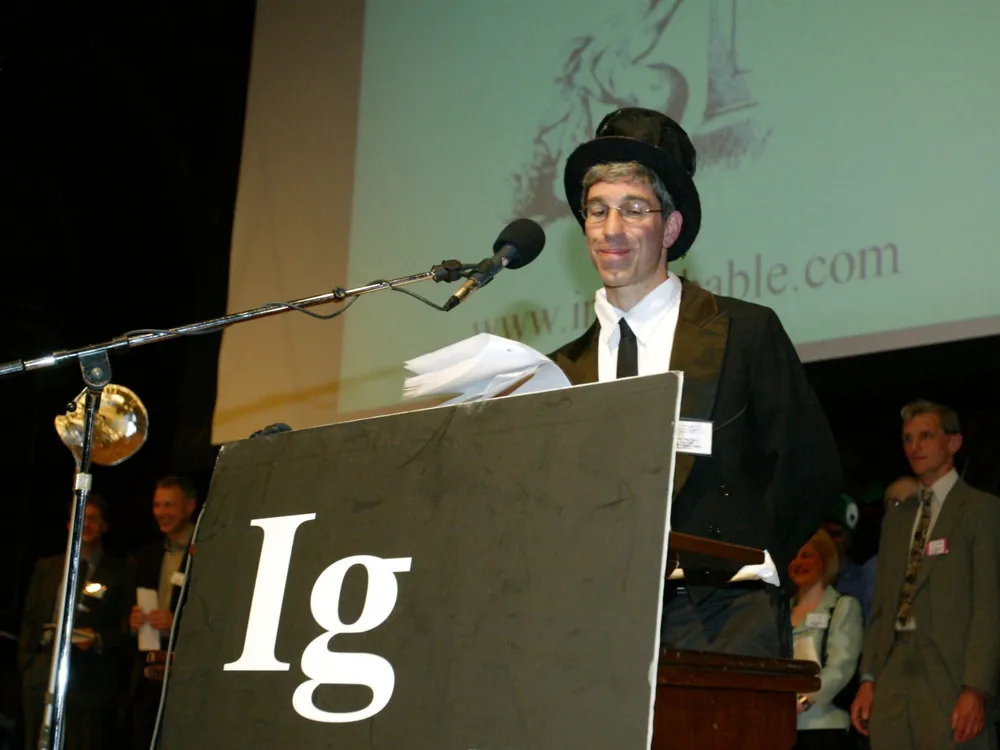 A man wearing a black suit and top hat stands at a podium