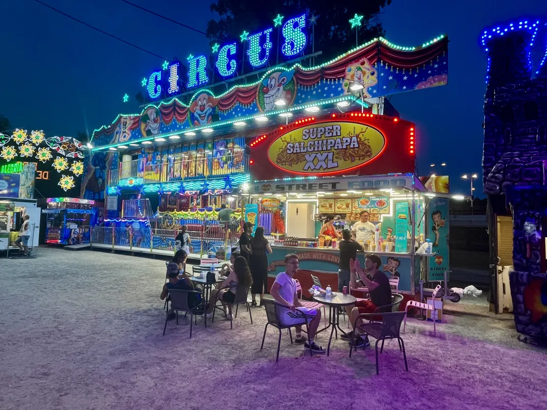 Patrons sit outside at a table at a carnival at night