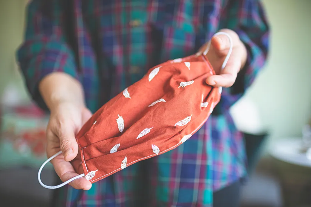 A person holds a sewn handmade fabric mask. 