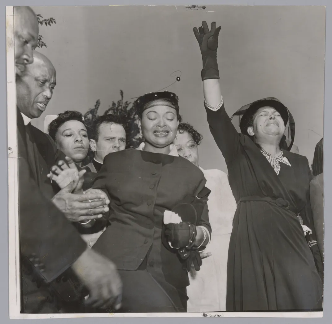 A black and white photograph of Mamie Till-Mobley, a woman in a black dress and hat, crying as she looks into her son's open casket, which is not visible