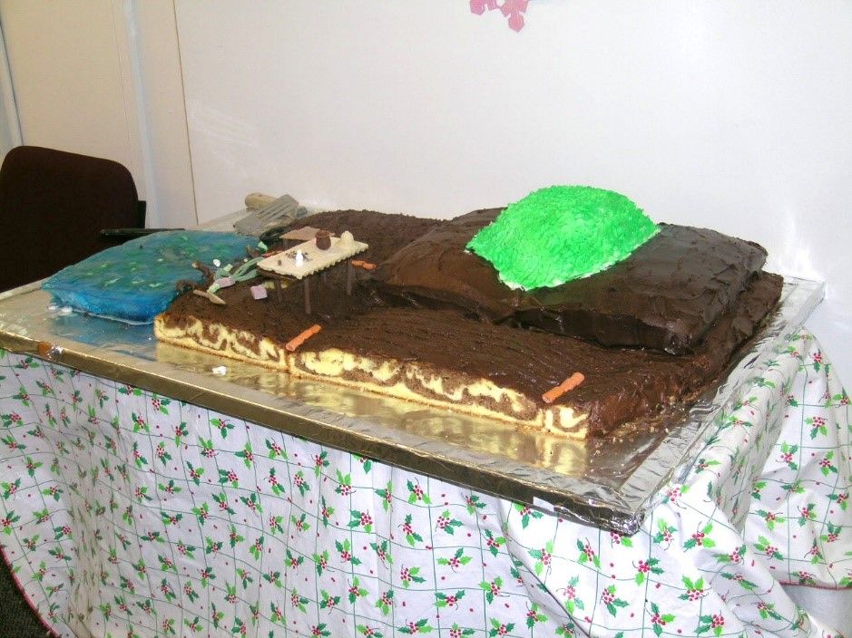 Brown and green chocolate longhouse made in the style of the Haida Native American tribe on a table with a white tablecloth with holly leaves. 