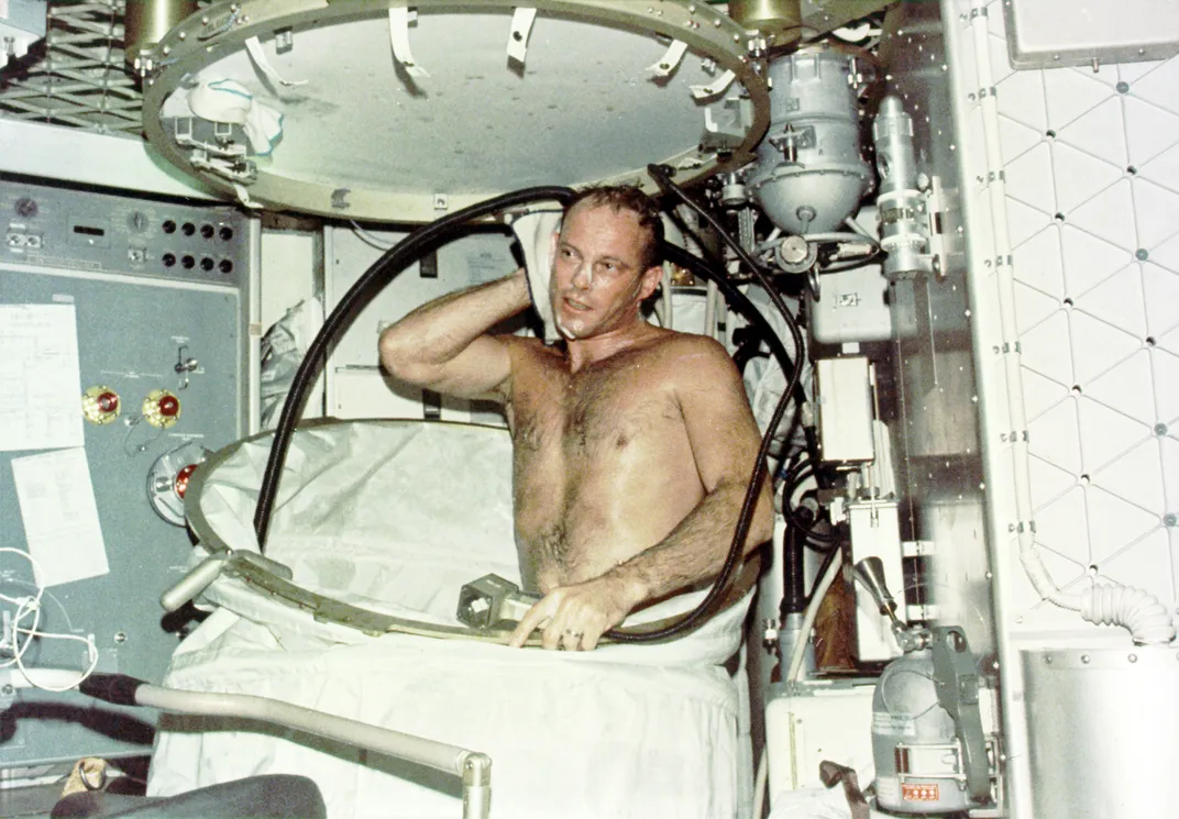 a shirtless man with soap on his face stands in the partially open shower with a towel
