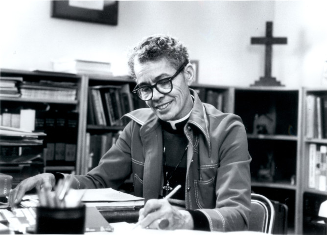 Pauli Murray sitting at a desk with a cross in the background