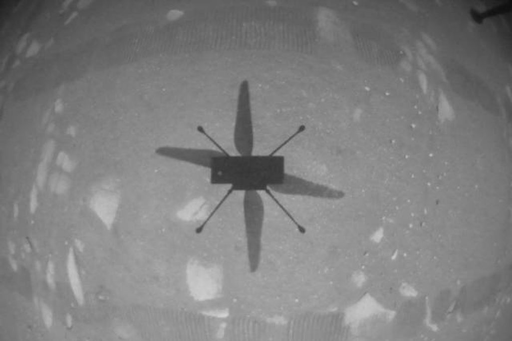 An image taken by the Mars Helicopter Ingenuity during it's first test flight. The image is black and white and shows the helicopter's shadow on the Martian surface.