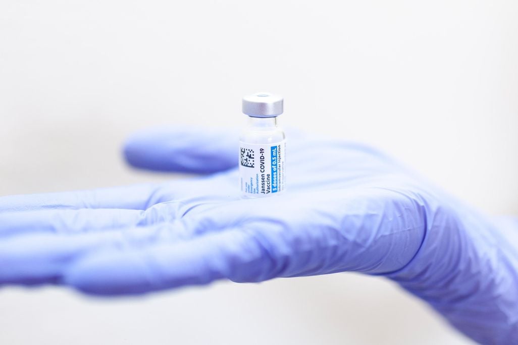 Blue gloved hand holds a small glass vial of Johnson and Johnson covid-19 vaccine